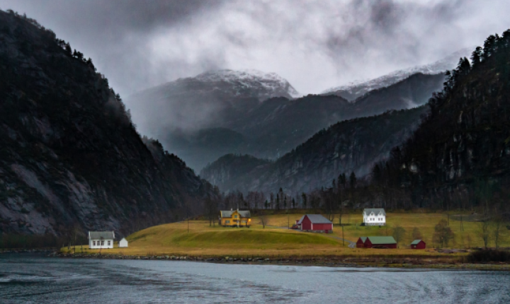 Hus i vannkanten mellom fjell. Foto: Michael Fousert på Unsplash